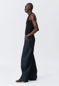 Labave tamnoplave traperice visokog struka s bočnim džepovima, uparene s crnim topom bez rukava i crnim sportskim cipelama.