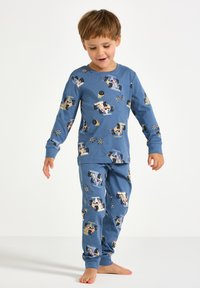 Lasten pyjamasetti sinisestä kankaasta, jossa on kilpa-autojen ja ruutulippujen kuvioita. Pitkät hihat ja housut, joissa on resorit nilkoissa.