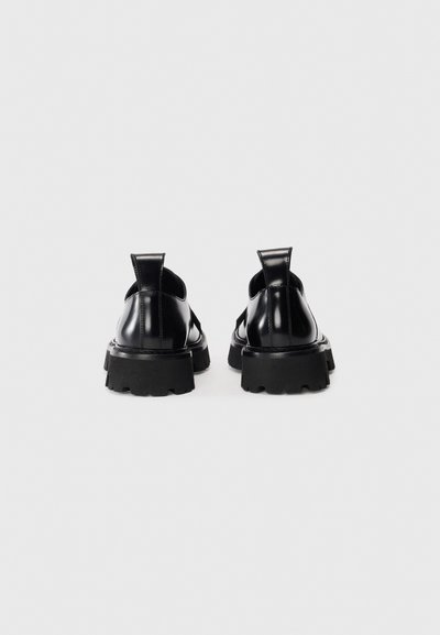 Black leather shoes with a chunky sole, featuring a smooth texture, round shape, and pull tabs at the heel for easy wearing.