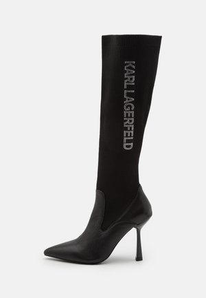 Knee-high black sock boot with a textured knit upper, pointed toe, and stiletto heel, featuring "KARL LAGERFELD" in rhinestones.