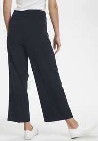 Wide-leg trousers in dark navy fabric with a smooth texture. Features a high waistband and two back pockets. Paired with white sneakers.