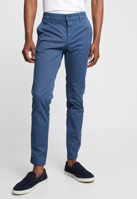 Herrens blå chinos i bomullsblandning med en figurnära design, slät textur, knappstängning och sidofickor, tillsammans med marinblå slipskor.