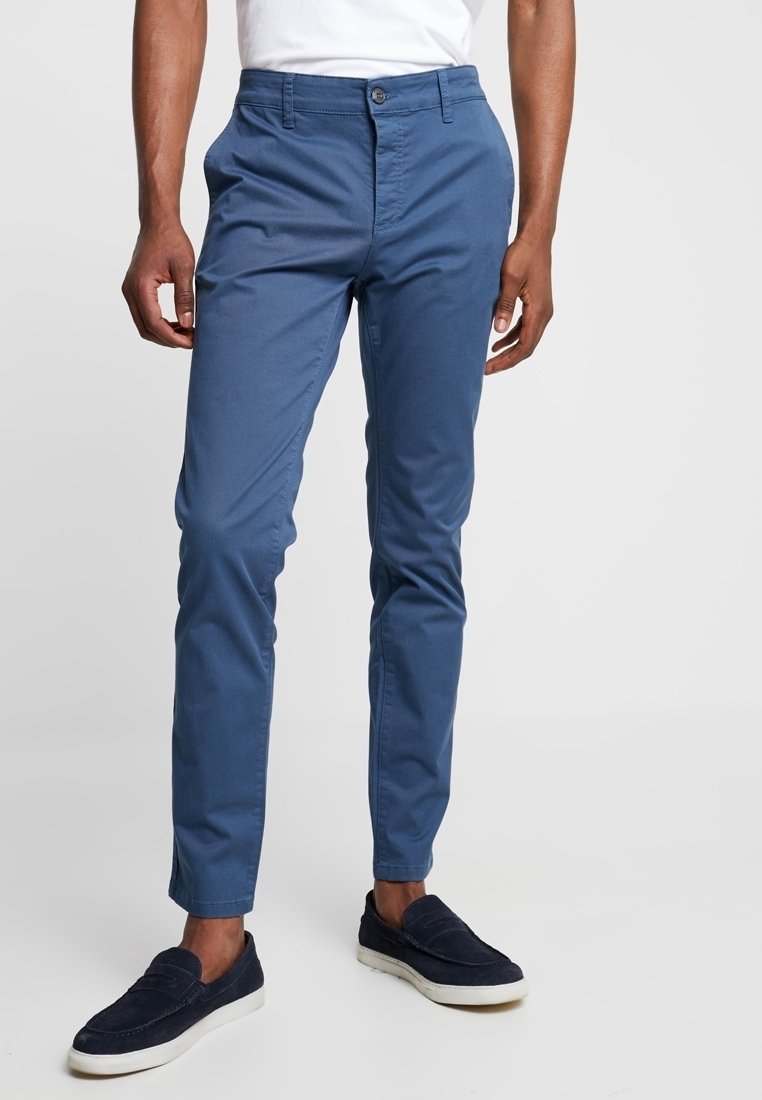 Herrens blå chinos i bomullsblandning med en figurnära design, slät textur, knappstängning och sidofickor, tillsammans med marinblå slipskor.