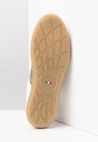 Semelle de chaussure en caoutchouc beige avec un motif texturé pour une meilleure adhérence ; comporte un logo circulaire et l'inscription « Fabriqué en Italie ». Partie supérieure blanche visible.