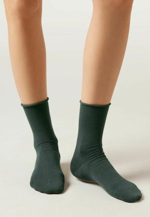 Dunkelgrüne Baumwollsocken mit einem gerippten Bündchen, glatter Textur und angepasster Form, die den Knöchel bis zur Mitte der Wade bedecken.