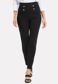 Hoge taille zwarte broek met een op maat gemaakte pasvorm, voorzien van twee goudkleurige knopen, zijnaad en een gladde textuur. Draagt met zwarte hoge hakken.