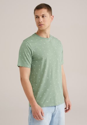 Camiseta de algodón verde con cuello redondo y mangas cortas, que presenta un patrón repetido de palmeras y conchas blancas en todo el diseño.