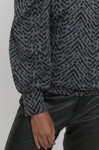 Grå sweater med struktureret sort chevron- og dyreprintmønster, med ballonsleeves og afslappet pasform. Sammen med sorte bukser.