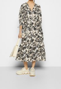 Kukkakuosiset midi-mekko vaaleassa, mustassa ja beigen värissä, jossa on v-pääntie, puffihihat ja kerrokselliset rypyt, yhdistettynä vaaleisiin lenkkareihin ja laukkuun.