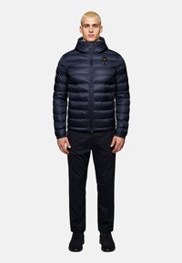 Navy puffer jacket with hood, zip closure, side pockets, and logo patch on chest. Smooth, lightweight material with quilted texture.