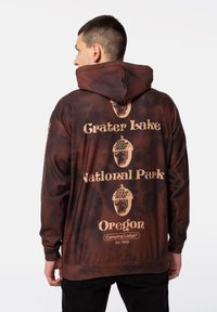 Brun batikhuva hoodie med texten "Grater Lake National Park" och Oregon i beige, med en grafisk ekollon-design och känguruficka.