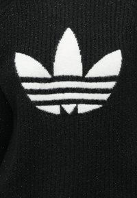 Suéter de malha preto com um proeminente logótipo trefoil branco da Adidas, apresentando três riscas horizontais no logótipo e uma superfície texturizada.