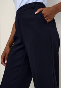 Pantalon bleu marine en tissu lisse, avec une taille ajustée, des poches latérales et une coupe droite. Lignes épurées et minimalistes.