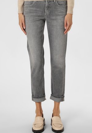 Grijze opgerolde spijkerbroek gedragen met beige instap loafers en een beige top met lange mouwen, getoond van taille tot voeten tegen een witte achtergrond.