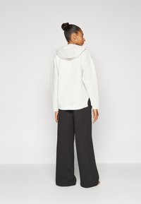 Sudadera blanca texturizada con capucha, combinada con pantalones oscuros de corte holgado en gris. El conjunto es simple y casual, con materiales suaves y cómodos.