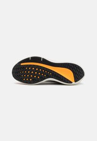 Suela de zapato con una textura de goma negra y acentos naranjas, forma redondeada y patrón de agarre para una tracción mejorada.