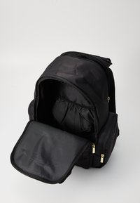 Juodas audinio kuprinės krepšys su dviem užtrauktukais, atverta sklendė atskleidžia vidines skiltis, minkšta tekstūra ir elastingos laikymo kišenės.