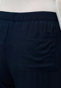Σκούρο μπλε παντελόνι με ελαστική μέση και πίσω τσέπη, φορεμένο με ανοιχτό μπεζ τοπ ορατό στη μέση.