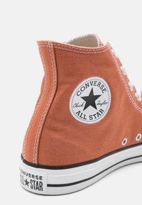 Baskets en toile couleur rouille avec semelle en caoutchouc blanc, ornées d'un patch logo étoile noir contrastant et de détails de couture blancs.