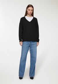 Czarny, oversize sweter w serek, noszony na białej bluzce, zestawiony z jasnoniebieskimi, wysokimi dżinsami. Miękka tekstura, casualowy styl, brak wyraźnych wzorów.