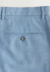 Pantalon en tissu bleu clair texturé vue de dos avec poche passepoilée boutonnée et deux passants de ceinture le long de la ceinture.