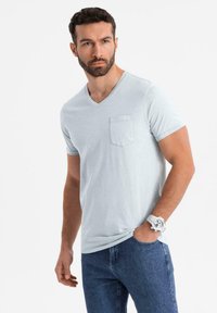 Světlezmodré bavlněné tričko s výstřihem do V a krátkými rukávy, se zapínáním na levé straně hrudi, doplněné tmavými džínami. K tomu stříbrné hodinky.