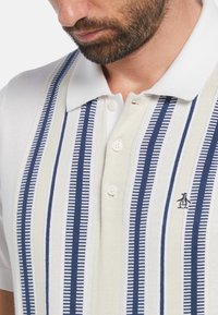 Poloshirt in Weiß mit vertikalen Streifen in Marineblau und Hellbeige. Mit Kragen, Knöpfen und einem Pinguin-Logo auf der Brust.