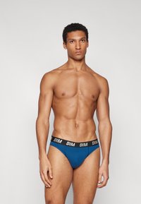 Blaue Baumwollslips mit einem schwarzen Bund, der das "DIM"-Logo trägt. Das Design ist enganliegend mit einer glatten Textur und minimalen Nähten.