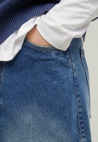 Denim jeans with a blue wash, visible stitching, and standard pockets, paired with a white t-shirt and ribbed navy sweater.