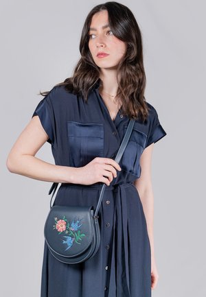 Sac bandoulière en cuir bleu foncé avec broderies florales et d'oiseaux, en forme ovale, texture lisse et sangle amovible.