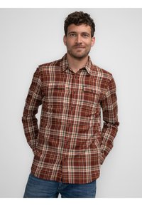 Camisa de cuadros en tonos rojos y marrones, con cuello, mangas largas y dos bolsillos en el pecho. Fabricada con un tejido texturizado.
