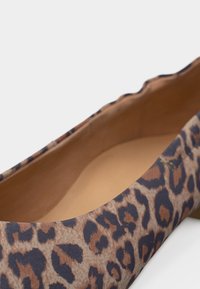 Κοντινό πλάνο ενός μπαλέτου με λεοπάρ σχέδιο, περιμετρικό κυματοειδές περίγραμμα και εσωτερική επένδυση σε καφέ απόχρωση.