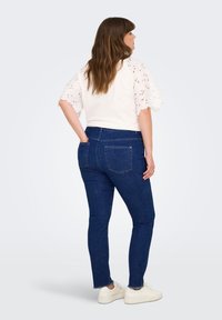 Modre skinny jeans iz denima s razfrkanim robom, v kombinaciji z belo majico z čipkastimi rokavi. Outfit dopolnjujejo bele superge.