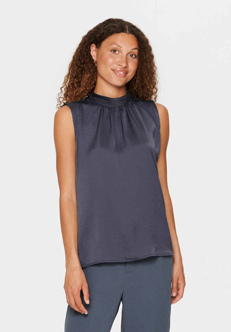 Blusa senza maniche blu navy con scollatura arricciata, texture liscia e orlo dritto. Abbinata a pantaloni scuri su misura.