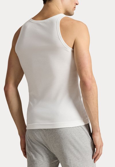 Λευκό βαμβακερό τοπ χωρίς μανίκια με στρογγυλή λαιμόκοψη και στενή εφαρμογή. Γκρι σορτς ορατά στη μέση, μινιμαλιστικό στυλ.