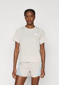 Αθλητικό πουκάμισο σε ανοιχτό μπεζ με κοντά μανίκια και μικρό λευκό λογότυπο. Συνδυάζεται με ανοιχτό μπεζ σορτς με μπλε πλαϊνές λεπτομέρειες. Ομαλή υφή.