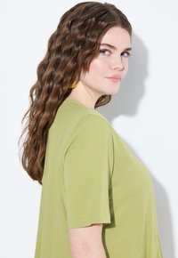 Olijfgroene t-shirt met korte mouwen en een losse pasvorm. Zachte textuur en ronde halslijn. Model heeft lang, golvend bruin haar.