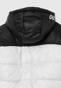 Czarna i biała pikowana kurtka z kapturem, o błyszczącym wykończeniu. Tył ma poziome szwy i biały napis „OUT”.