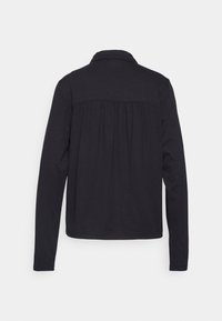Chemise noire à manches longues avec col et détail de tissu froncé sur le haut du dos, vue de dos sur un fond uni.