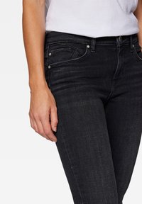 Jeans de mezclilla negra con un corte ajustado, que cuentan con cinco bolsillos, detalles de herrajes plateados y costuras sutiles en la parte frontal.
