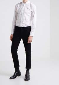 Weißes Hemd mit dezenten grauen Muster, kombiniert mit schwarzen, eng anliegenden Hosen und schwarzen Leder-Stiefeletten. Hochgerollte Hosenumschläge.