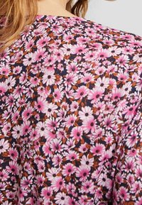 Blommig blus med marin bakgrund, prydd med rosa och vita tusenskönor med bruna detaljer. Lätt, mjukt material, rund halsringning, kort ärm.