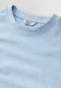 T-shirt bleu clair à col rond avec étiquette de marque "NEXT" et texte "Relaxed Fit" visible sur l'étiquette du col.