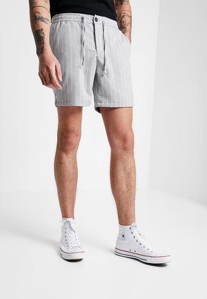 Shorts a rayas grises con cintura elástica y detalle de cordón, combinados con zapatillas altas blancas. Textura de tela suave.