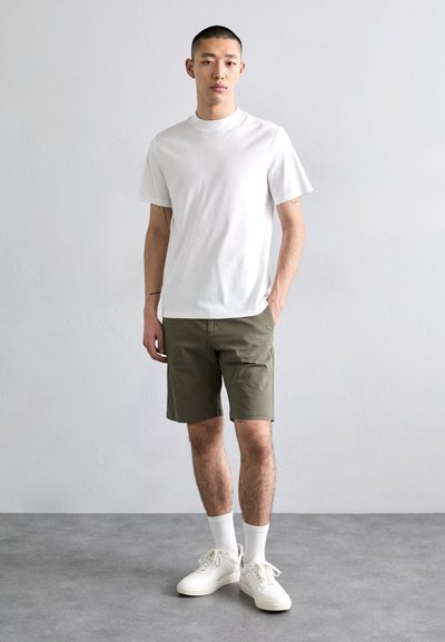 T-shirt en coton blanc, shorts vert olive, baskets blanches et chaussettes blanches. Coupe décontractée, texture lisse, design simple, sans motifs visibles.