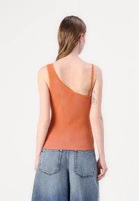 Ribbelachtig oranje tanktop met een enkel-schouder ontwerp, gecombineerd met high-waisted denim shorts met een brede pijp en achterzakken.