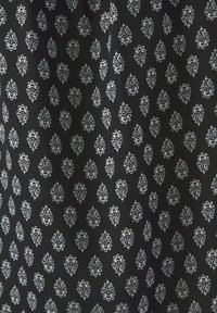 Tissu noir arborant un motif floral blanc répétitif avec des détails complexes, créant un effet texturé. Convient pour des vêtements ou des décorations.