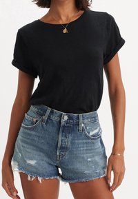 Black cotton T-shirt with rolled sleeves paired with distressed denim shorts. Shorts feature frayed hem, blue fading, and multiple pockets.