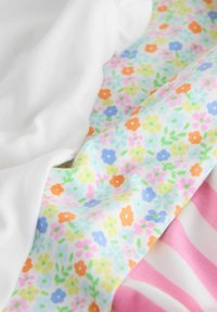 Tejido suave con estampado de pequeñas flores blancas y multicolores, y franjas horizontales rosas y blancas, mostrado en pliegues de cerca.