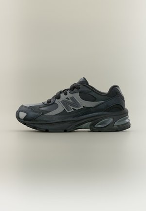 Baskets de sport New Balance noires et gris foncé à lacets avec semelle rembourrée montrées en profil sur fond neutre.